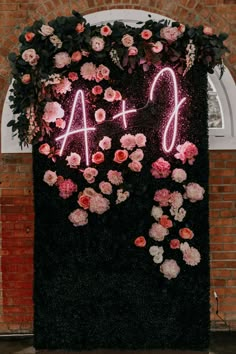 a sign that says ao and surrounded by flowers on the side of a brick wall