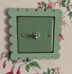 a green light switch cover sitting on top of a flowery wallpaper covered wall