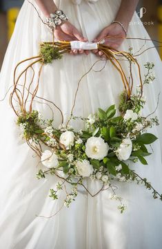 a woman in a white dress holding a flower crown with greenery and flowers on it