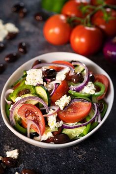 a salad with tomatoes, olives, cucumbers and feta cheese in a white bowl