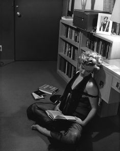 a woman sitting on the floor in front of a bookshelf reading a book