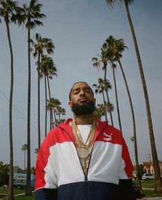 a man standing in front of palm trees wearing a red, white and blue jacket