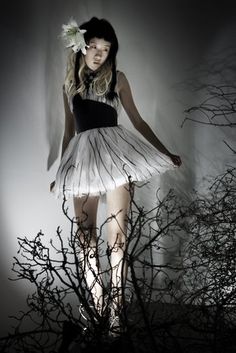 a woman in a white and black dress standing next to some branches