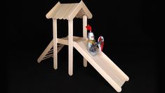 a wooden play set with a slide and sand bucket on it's side, against a black background