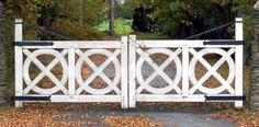 an image of a white gate in front of some trees and leaves on the ground