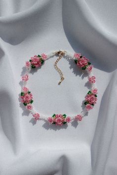 a bracelet with pink flowers on it and a gold cross in the middle is laying on a white cloth