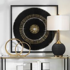 a black and gold table lamp sitting on top of a wooden shelf next to a framed art piece