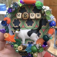 a hand holding up a small cat made out of beads and other items with words meow written on it