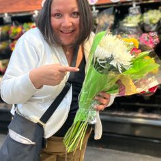 a woman pointing at flowers in a flower shop with her thumb up to the camera