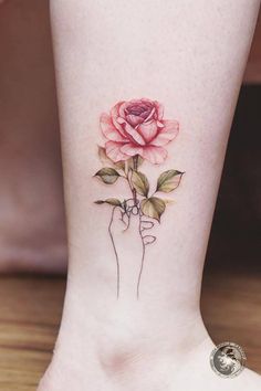 a small rose tattoo on the ankle is shown in this close up photo, it has pink flowers and green leaves