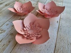 three pink paper flowers sitting on top of a wooden table