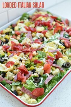 a salad with tomatoes, olives and lettuce in a red dish on a counter