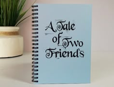 a blue notebook with the words a tale of two friends written on it next to a potted plant