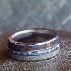 two wedding bands with blue and gold inlays on them sitting on a rock