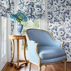 a blue and white chair sitting in front of a window next to a vase with flowers on it