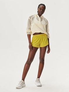 a woman in yellow shorts and a white shirt is standing with her hands on her hips