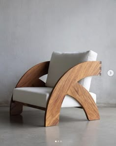 a modern chair made out of wood and white upholstered fabric, in front of a gray wall