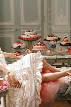 two women sitting in chairs with cakes and cupcakes on the table