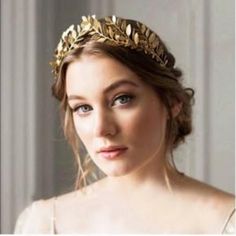 a woman wearing a gold leaf headpiece in front of a white wall and window