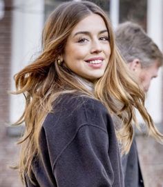 a woman with long hair standing in front of a brick building smiling at the camera