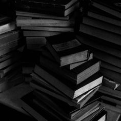 a pile of books sitting next to each other on top of a wooden table in black and white