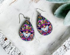 a pair of colorful earrings sitting on top of a wooden table next to a plant