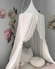 a white canopy bed in a bedroom with flowers on the wall and behind it is a round pillow