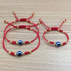 two red string bracelets with gold beads and blue glass eyes on each strand, sitting on a wooden surface