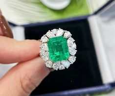 an emerald and diamond ring being held by someone