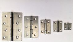 four metal hinges are lined up on a white surface