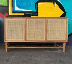 a wooden cabinet with wicker doors in front of a colorful wall painted with graffiti