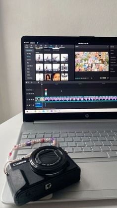 an open laptop computer sitting on top of a white table next to a small camera