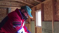 a man in a red jacket and green hat working on the inside of a building