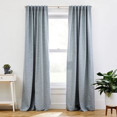 a room with a white table and blue curtains on the window sill, next to a potted plant