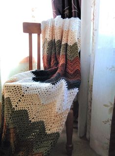 a crocheted blanket sitting on top of a wooden chair next to a window