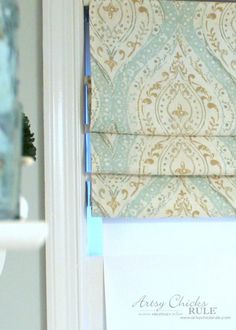 an open window with roman shades on the outside and inside, in front of a white door