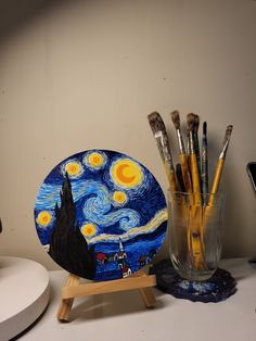 a table topped with art supplies next to a vase filled with paint and pencils