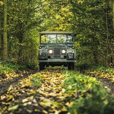 an army truck driving down a dirt road in the middle of some trees and leaves