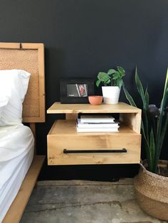 a nightstand with books and plants on it next to a bed