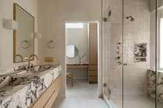 a bathroom with marble counter tops and two sinks in front of a shower stall that has mirrors on the wall