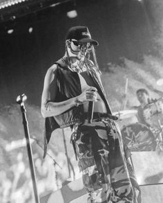 a man standing on top of a stage holding a microphone in his hand and wearing a hat