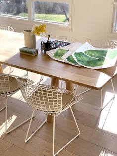 a wooden table topped with two white chairs next to a book on top of a hard wood floor