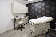 a medical room with an exam table and chairs in it, along with cabinets on both sides