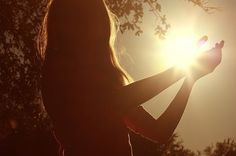 the silhouette of a woman holding her hands out in front of the sun