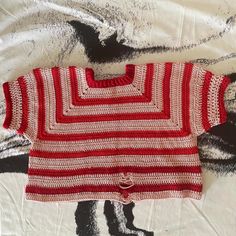 a red and white knitted sweater laying on top of a bed next to a painting