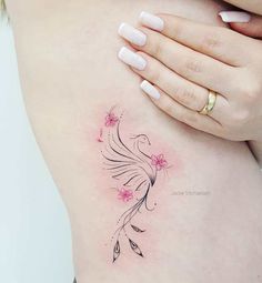 a woman's stomach with pink flowers and feathers tattoo on her left side ribcage