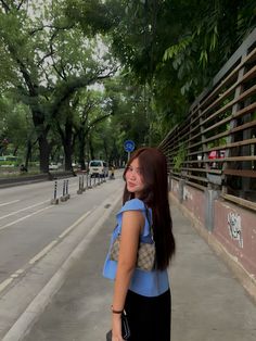 a woman standing on the side of a road with trees in the backgroud