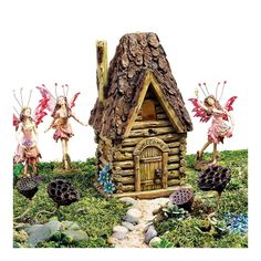 three fairy figurines in front of a small log cabin with flowers and rocks