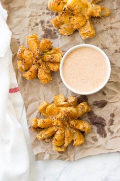 some fried food is on a piece of paper next to a bowl of dipping sauce