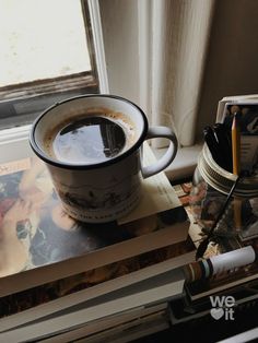 a cup of coffee sitting on top of a stack of books next to a window